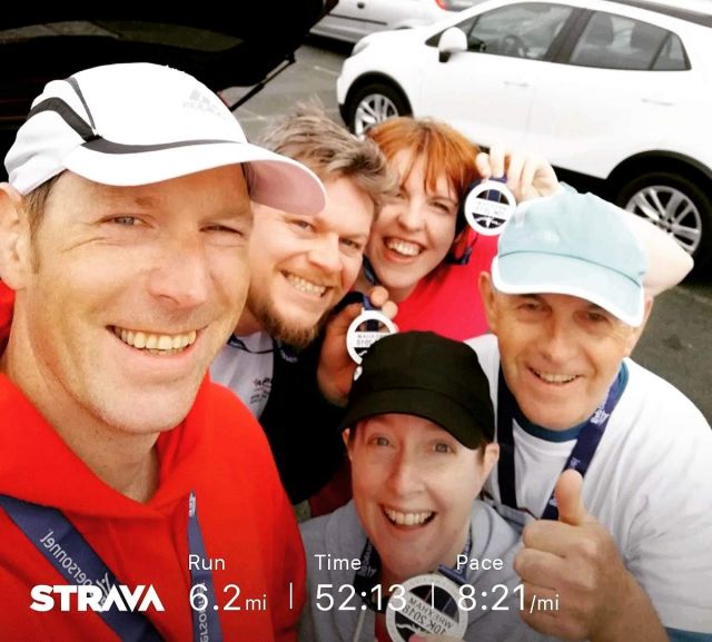 5 people standing in a car park smiling at the camera and holding up their medals. The text at the bottom says run: 6.2 miles, time 52:13, pace 8:21/mile