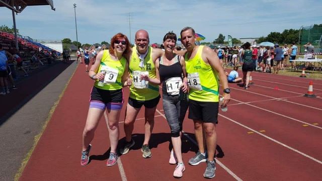 Four runners stand on a track smiling into the camera