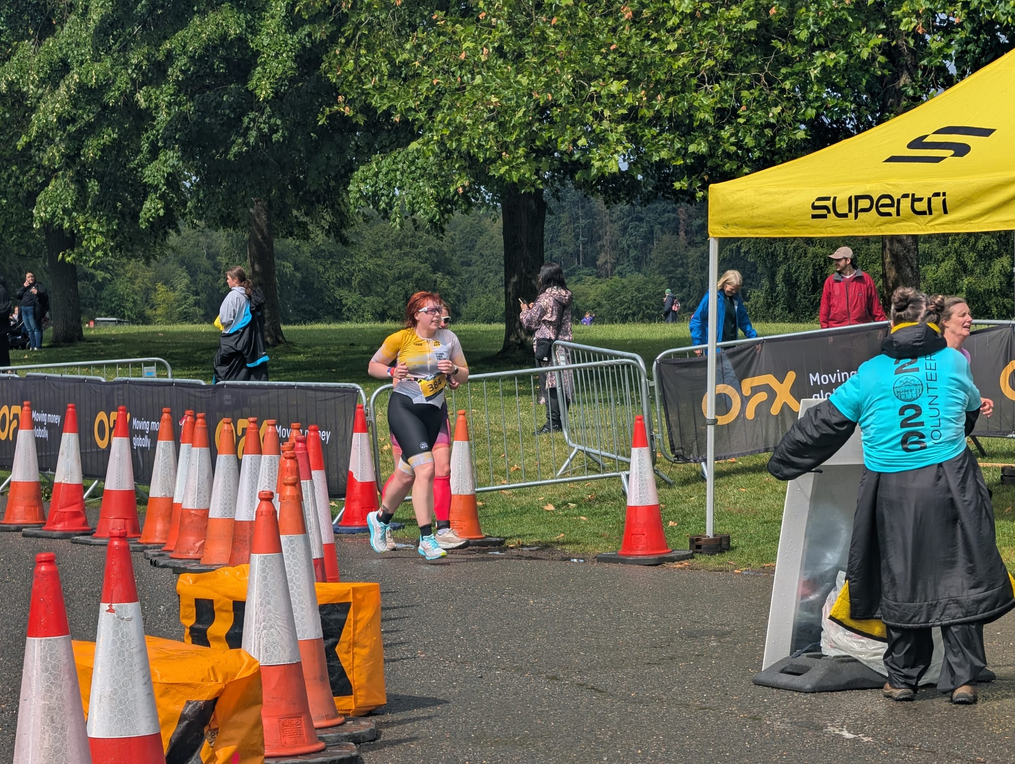 Me wearing a yellow and black women in tri UK trisuit running past some cones on the Blenheim Palace Triathlon run course